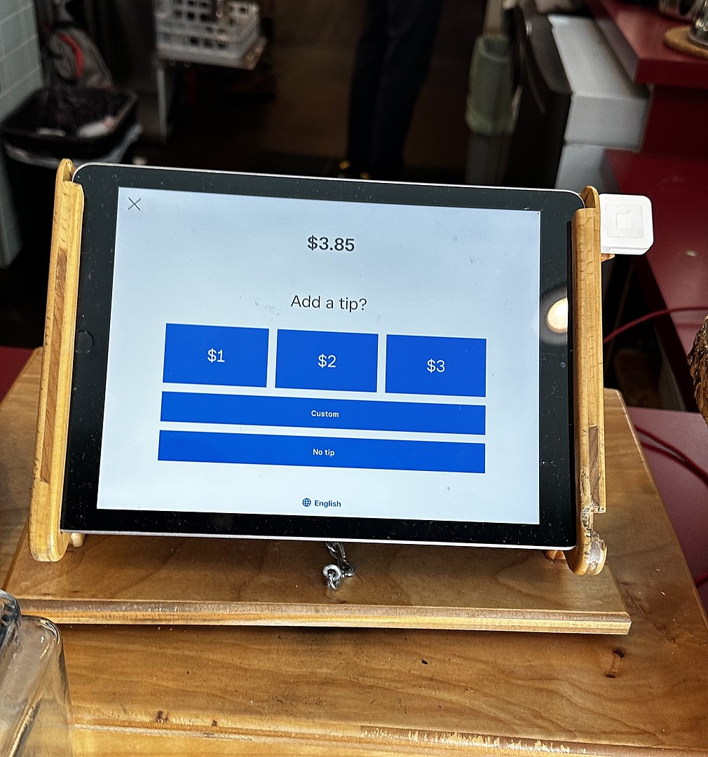 An “Add a tip” screen at a coffee shop after paying for a $3.85 coffee, with suggested amounts of $1 (just over 25%), $2 (just over 50%), and $3 (just under 78%) tips. Custom tip and giving no tip at all is also enabled. Taken in San Francisco, California.